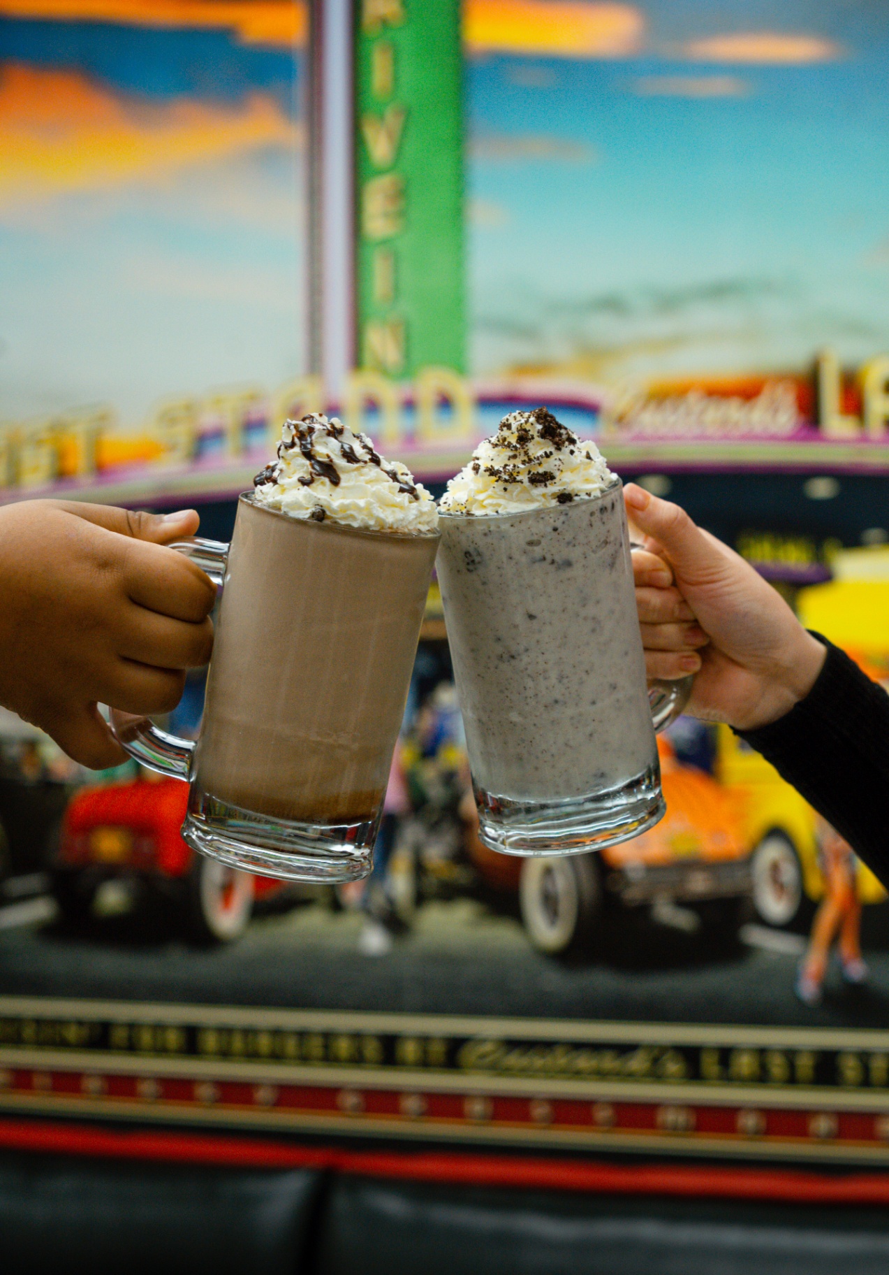 Two hand-spun shakes cheers'd in front of a classic diner mural